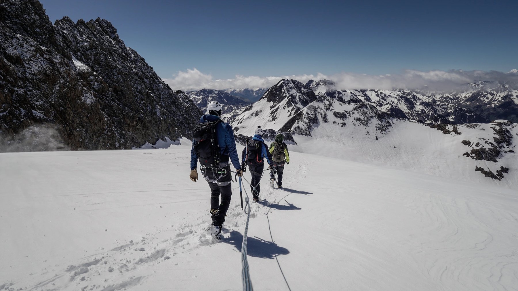 Seilschaft von Bergsteigern in weitläufiger, verschneiter Berglandschaft